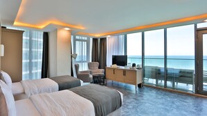 A modern hotel room with a large bed, a desk, a chair, and a TV. The room has large windows with a view of the ocean. - Batumi View Luxury  (Batumi)