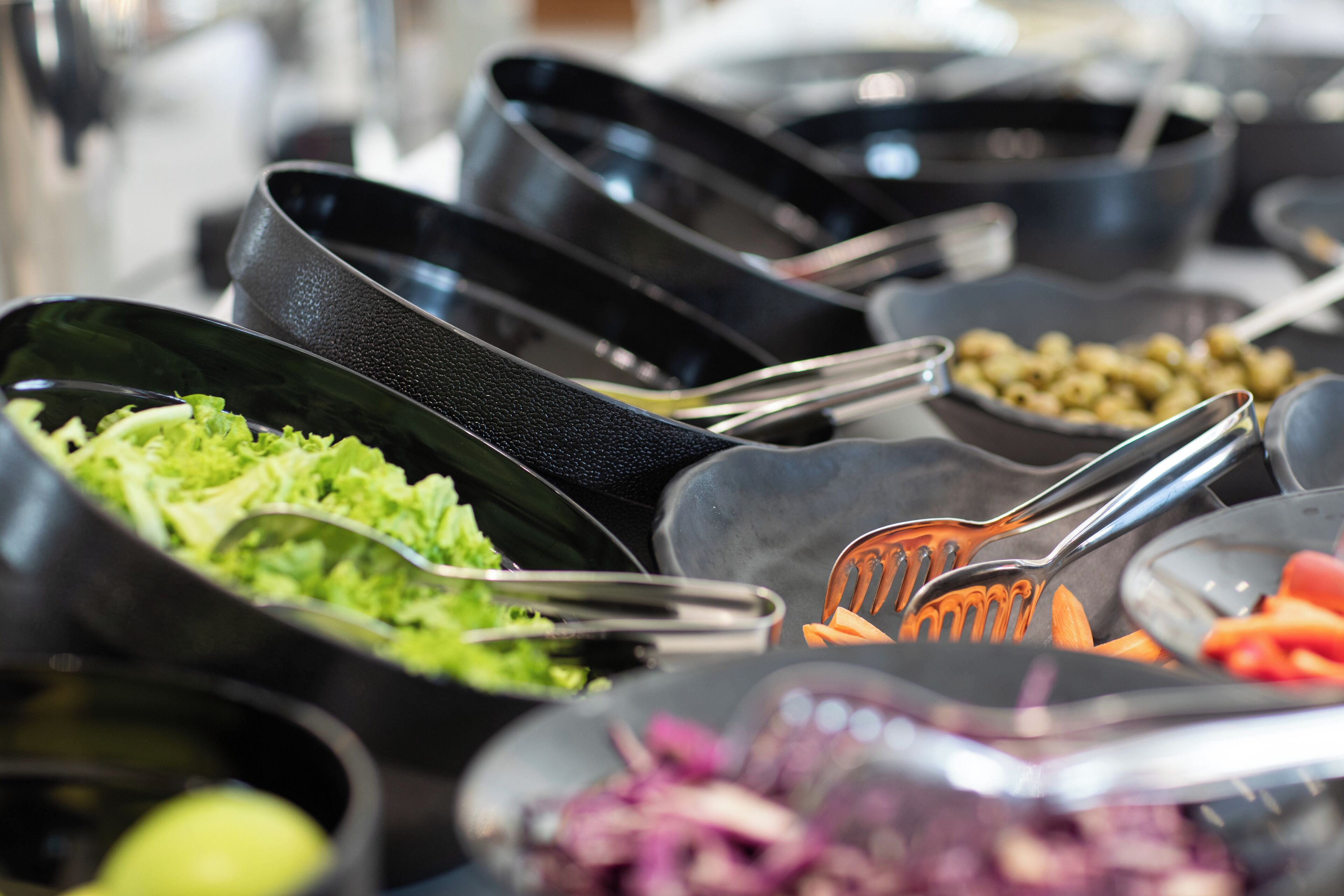 Un bufé con diversos platos, incluyendo ensalada, aceitunas y verduras.