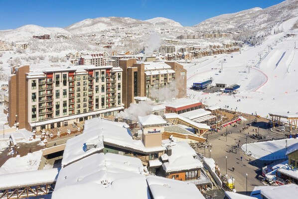 A snow-covered resort with multi-story buildings, a ski lift, and a snowmobile rental area.