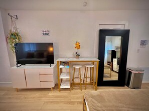 A compact living space with a TV, a small dining area, and a mirror reflecting a kitchenette.
