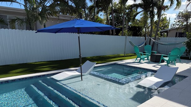 Una piscina con agua cristalina, una sombrilla azul y sillas verdes.