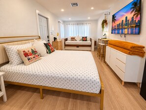 A modern bedroom with a bed, a desk, and a painting of a cityscape.