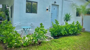 Un edificio blanco con una puerta identificada con el número 2, una ventana y un pequeño patio con mesa y sillas.