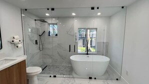 A modern bathroom with a glass-enclosed shower, a freestanding bathtub, and a toilet.