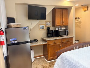 A compact kitchenette with a refrigerator, microwave, coffee maker, and a flat-screen TV mounted on the wall.