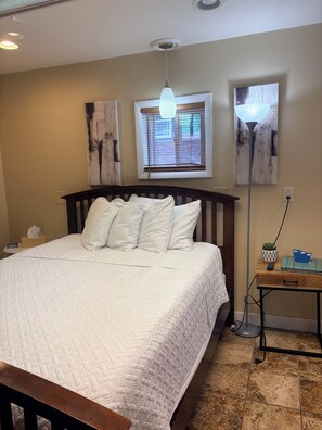 A bedroom with a bed, bedside table, lamp, and artwork on the wall. - Stay In Ohiopyle by the trail with a jetted tub (Ohiopyle)