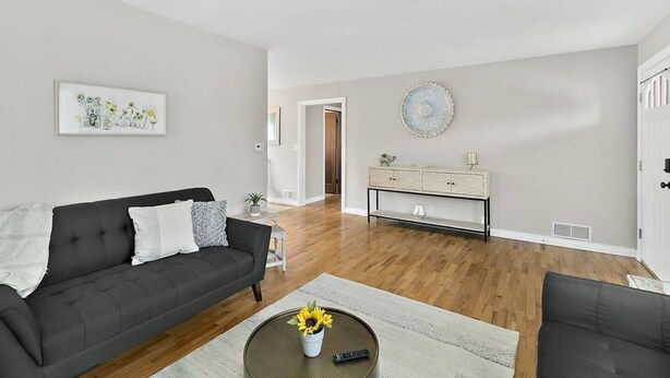 Una sala moderna con un sofá gris oscuro, una mesa de centro blanca con un girasol y una consola de color claro con objetos decorativos.