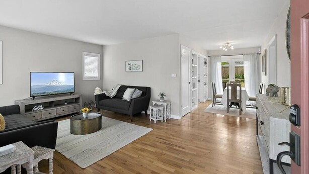 Een moderne woonkamer met een flatscreen televisie, een donkere bank, een salontafel en een eethoek met een tafel en stoelen.