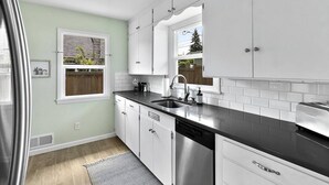 Een moderne keuken met witte kastjes, een zwart aanrecht en een RVS vaatwasser.