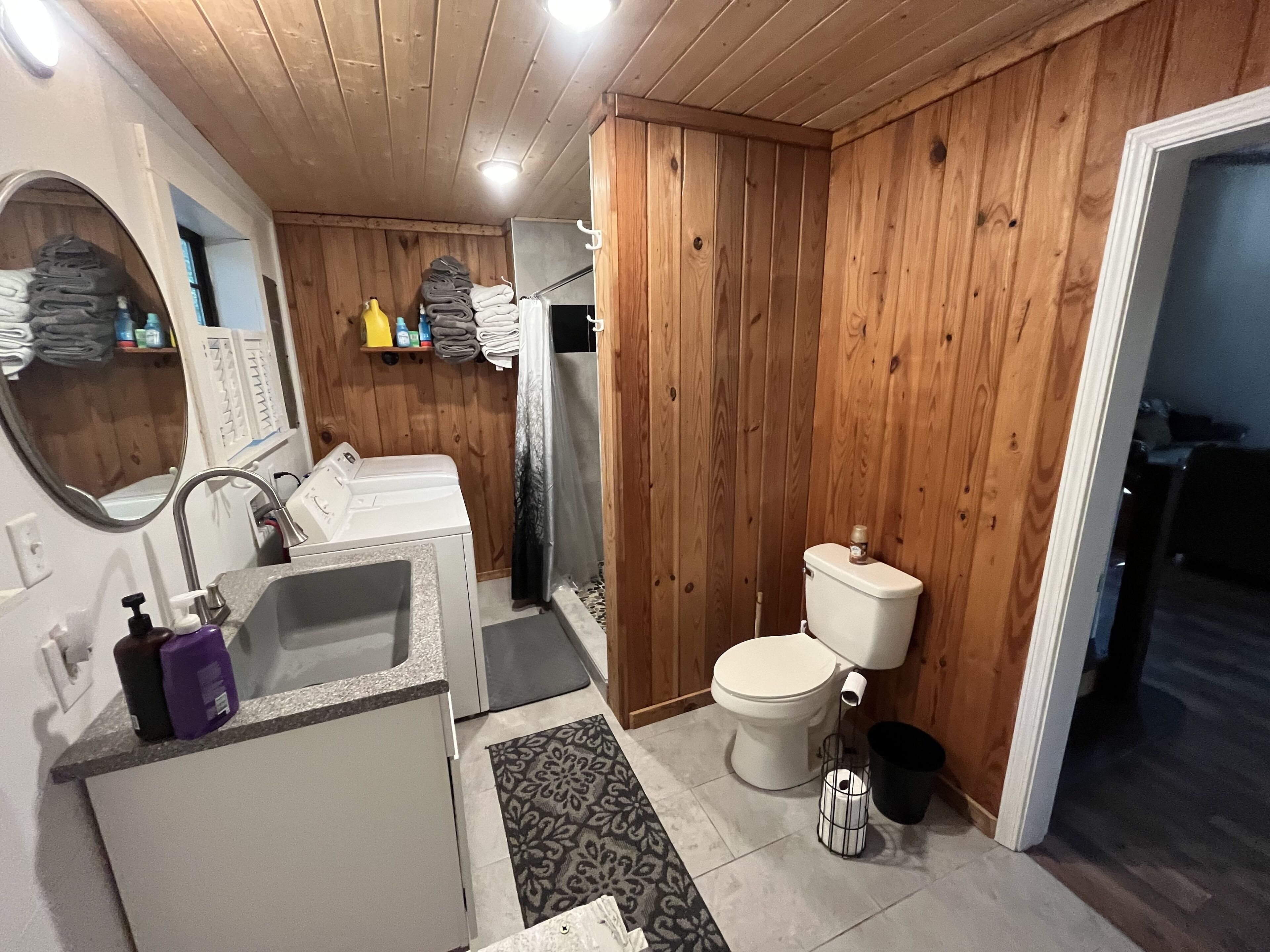 Un baño pequeño con paredes de madera, un inodoro blanco, un lavabo con espejo y una zona de ducha.