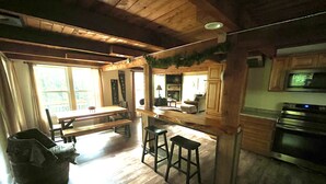 Una cocina amplia con vigas de madera, un comedor con banco y vistas al exterior a través de ventanas grandes.