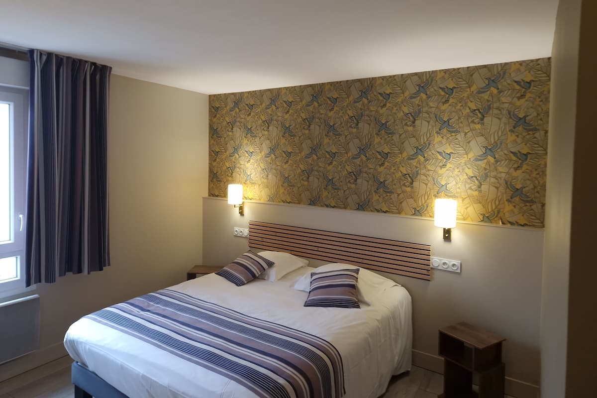 Een net opgemaakt bed met gestreept beddengoed, twee bedlampjes en een muur met een vogelmotief.