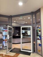 Entrada de un hotel con mostrador de recepción, puertas de vidrio y varios avisos.