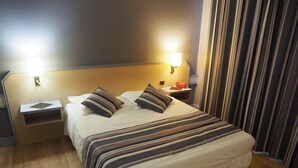 Een net opgemaakt bed met gestreept beddengoed, een nachtkastje met een lamp en een nachtkastje met een boek.
