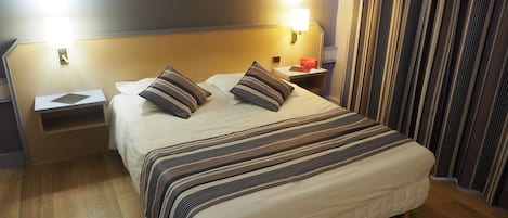 A neatly made bed with striped bedding, a bedside table with a lamp, and a nightstand with a book.