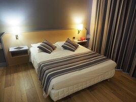 Una cama bien hecha con ropa de cama a rayas, una mesita de noche con una lámpara y un atril con un libro.