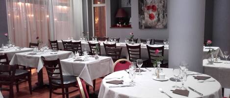 A restaurant with multiple round tables, each set with cutlery, glasses, and a vase with a single flower.