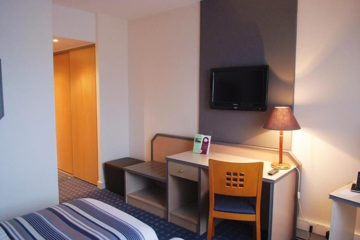 Une chambre d’hôtel équipée d’un lit, d’un bureau, d’une chaise, d’un téléviseur fixé au mur et d’une lampe.