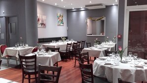 Een eetgedeelte met ronde tafels voor vier personen, elk met een witte tafelkleed, stoelen en servies.