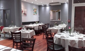 Un comedor con mesas redondas dispuestas para cuatro comensales, cada una con mantel blanco, sillas y vajilla.