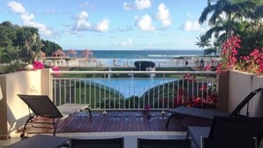 Een terras met loungestoelen met uitzicht op een zwembad en strand.