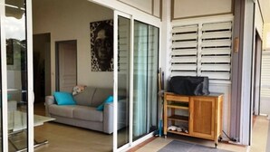 Een woonkamer met een bank, een bijzettafeltje en een schuifdeur die uitkomt op een balkon.