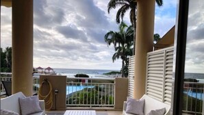 Een balkon met witte meubels, uitzicht op de oceaan en palmbomen.