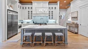 Un'ampia cucina con armadietti bianchi, un'isola grande con sgabelli da bar, un frigorifero in acciaio inossidabile e un soffitto in legno.