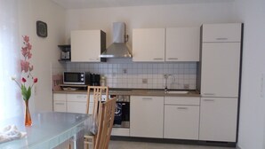 A compact kitchen with white cabinets, a microwave, a stove, and a sink. There is a dining table with chairs and a vase with flowers. - 2 bedroom private vacation home in wurster nordseekã¼ste (Wurster Nordseeküste)