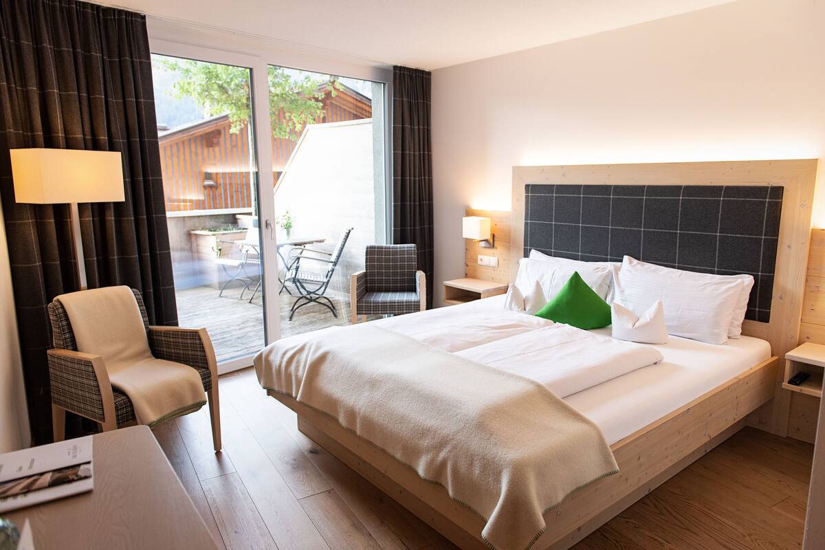 Quarto de hotel com uma cama grande, uma cadeira, uma escrivaninha e vista para o exterior.