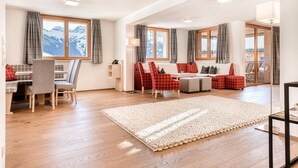 A spacious living room with a wooden floor, a large rug, and a seating area with red and grey chairs. - Spa-Hotel DAS SCHÄFER (Fontanella)