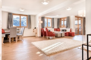 Amplia sala de estar con piso de madera, un tapete grande y una zona de estar con sillones rojo y gris.