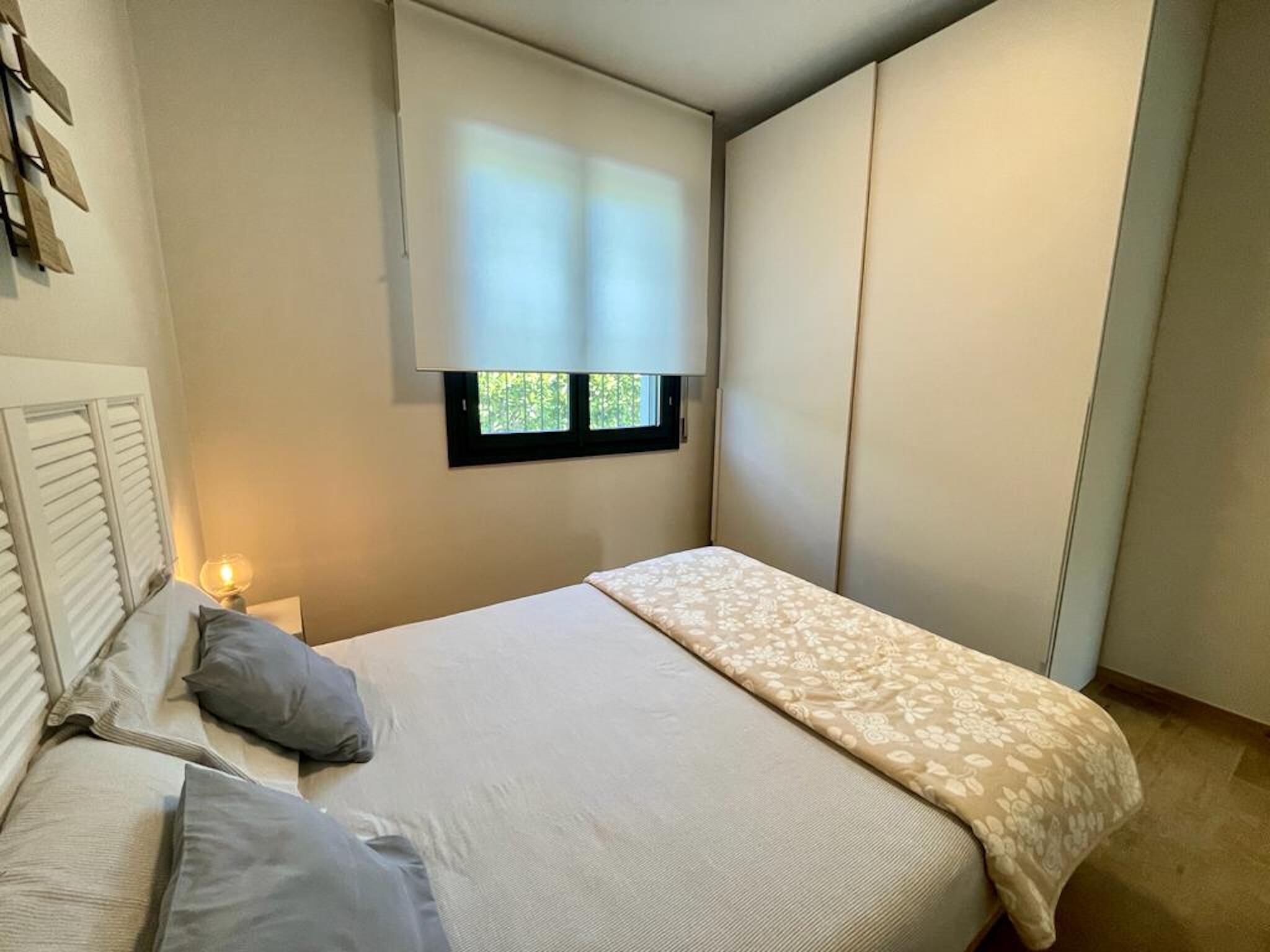 A bedroom with a bed, bedside table, lamp, window, and built-in wardrobe.