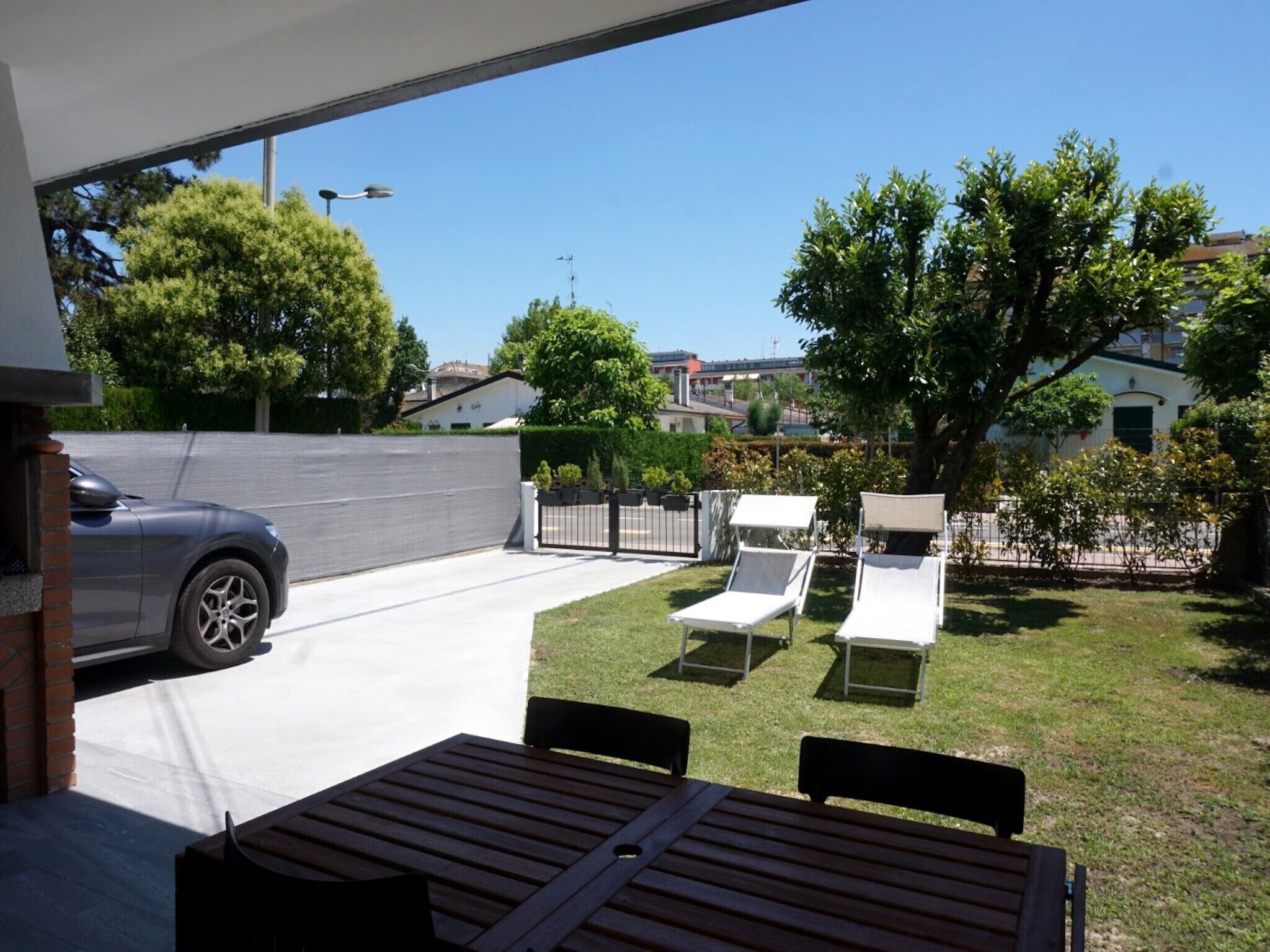 Un patio con mesa y sillas, un coche estacionado en la entrada y vistas del barrio.