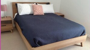 Una cama individual con estructura de madera, una colcha azul marino y dos almohadas.