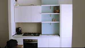 Una cocina compacta con armarios blancos, una estufa a gas y una cafetera.
