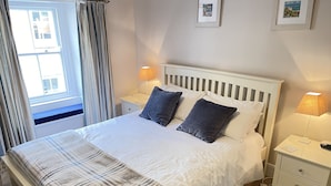 A neatly made bed with a white and plaid bedspread, two dark pillows, and two bedside lamps. - Howards Way - a cottage that sleeps 5 guests in 2 bedrooms (St Ives)