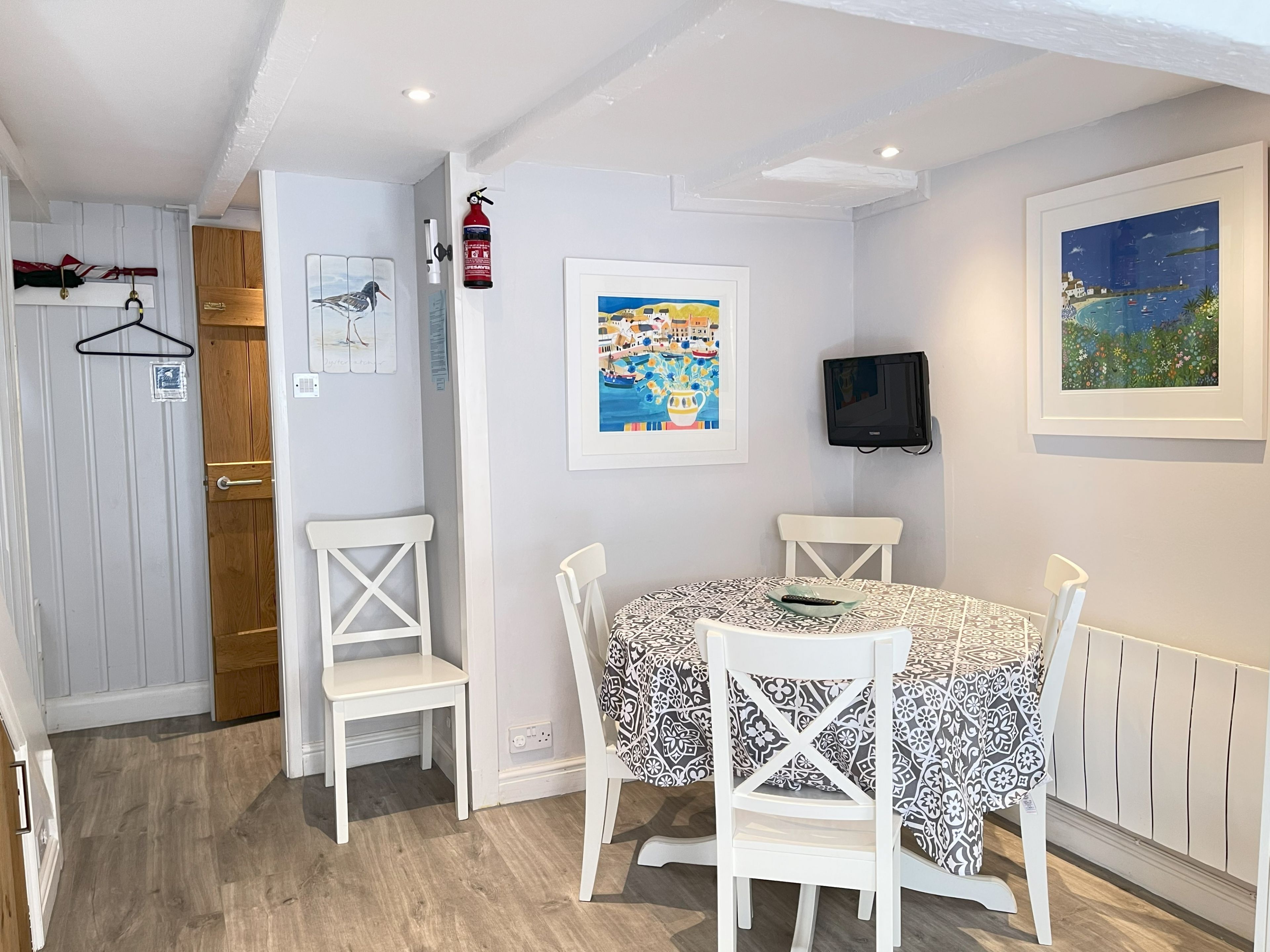 A dining area with a table and chairs, a fire extinguisher, and a framed painting on the wall.