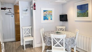 A dining area with a table and chairs, a fire extinguisher, and a framed painting on the wall. - Howards Way - a cottage that sleeps 5 guests in 2 bedrooms (St Ives)