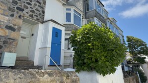 A stone facade with a blue door, a white wall, and a large bush in front. - 10 The Warren - a cottage that sleeps 5 guests in 3 bedrooms (St Ives)
