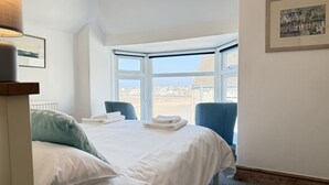 A hotel room with a bed, a chair, a window with a view of buildings, and a framed picture on the wall. - 10 The Warren - a cottage that sleeps 5 guests in 3 bedrooms (St Ives)