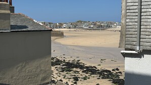 A coastal view with a sandy beach, rocky shoreline, and a row of buildings in the background. - 10 The Warren - a cottage that sleeps 5 guests in 3 bedrooms (St Ives)