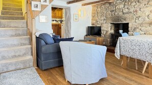 A cozy living room with a staircase, a stone fireplace, a TV, and a dining area. - 10 The Warren - a cottage that sleeps 5 guests in 3 bedrooms (St Ives)