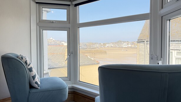 A corner room with a large bay window overlooking a beach and buildings. - 10 The Warren - a cottage that sleeps 5 guests in 3 bedrooms (St Ives)