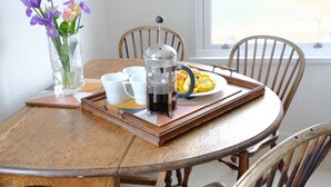 Una mesa de comedor de madera con una cafetera, un plato de comida y un jarrón con flores.