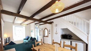 A dining area with a wooden table and chairs, a green sofa, and a staircase leading to a kitchen area. - Silver Seahorse - a cottage that sleeps 6 guests in 3 bedrooms (St Ives)