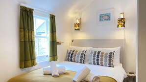 Una cama bien hecha con almohadas estampadas, una mesita de noche con lámpara y una ventana con cortinas.