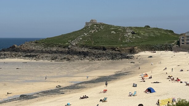 Una playa con una colina al fondo, costa rocosa y gente tomando el sol.