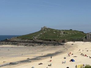 Une plage avec une colline en arrière-plan, un rivage rocheux et des gens qui prennent un bain de soleil.