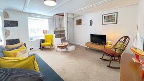 Una sala moderna con un sofá, un sillón amarillo, un televisor, un mueble de madera y una escalera.